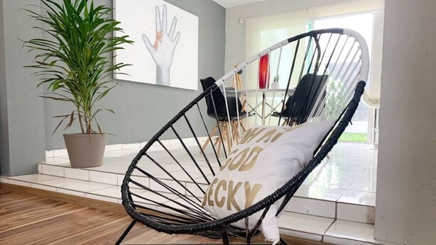 A room with a wicker chair, a potted plant, and a view of the outdoors. - Charming House Rental in Zapopan, Mexico - Your Private Oasis (Zapopan)
