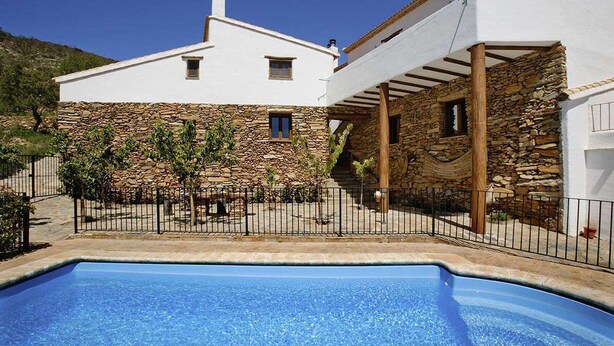 Ein modernes Haus mit Naturstein-Fassade, einem Pool und einer Pergola.