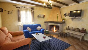 Ein Wohnzimmer mit Kamin, einem blauen Sofa, einem braunen Sessel und einem an der Wand befestigten Fernseher.