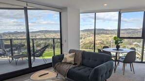 Een moderne woonkamer met een donkerblauwe bank, een kleine ronde tafel en een balkon met uitzicht op een stadsgezicht.