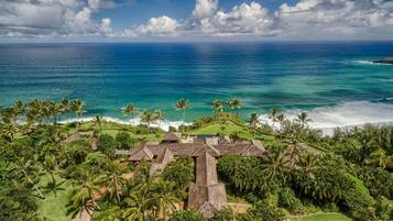 A tropical resort with multiple thatched-roof buildings, lush greenery, and a view of the ocean.