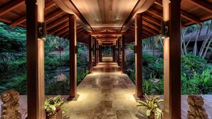 A covered walkway with wooden beams and columns, flanked by lush greenery and a water feature. - Hale Ae Kai in Kilauea (Kilauea)