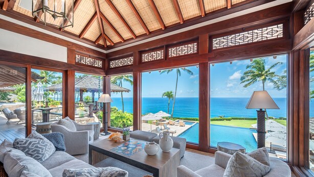 A luxurious room with a large window overlooking a pool and the ocean. There is a sofa, a coffee table, and a lamp. - Hale Ae Kai in Kilauea (Kilauea)