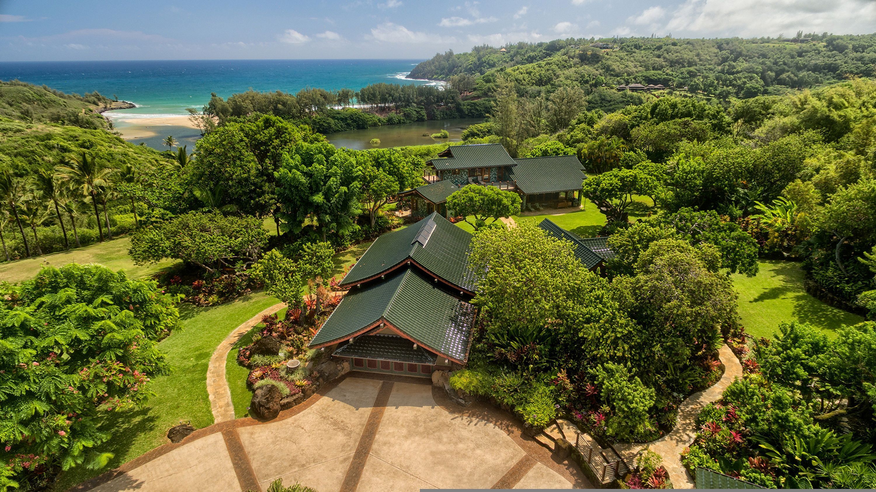 A traditional Japanese-style building with a green roof, surrounded by lush greenery and a view of the ocean.