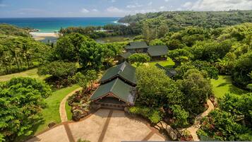 A traditional Japanese-style building with a green roof, surrounded by lush greenery and a view of the ocean.