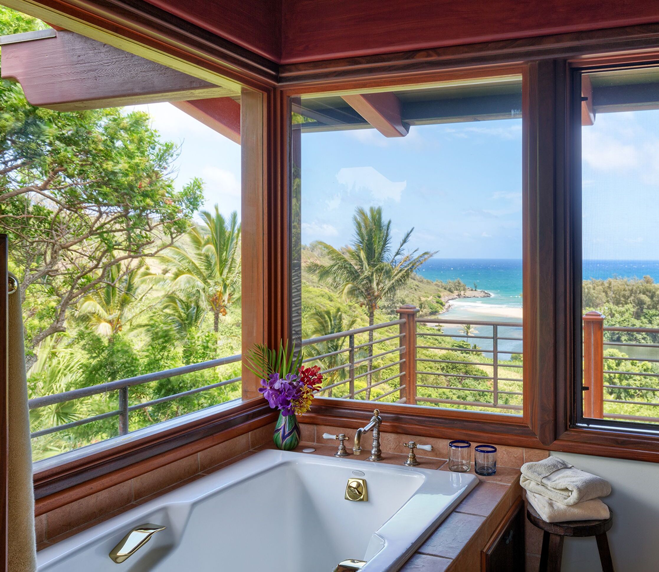 Un baño con una bañera grande, una ventana con vistas al océano y un taburete pequeño con una toalla.