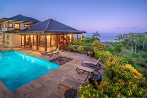 A two-story house with a swimming pool, outdoor seating, and a view of the ocean.