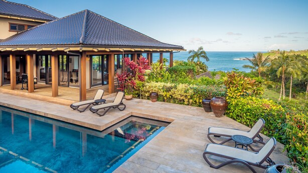 A poolside area with lounge chairs, a covered patio, and a view of the ocean. - Ikena Lani in Kilauea (Kilauea)