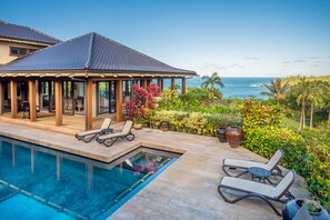Ein Poolbereich mit Liegestühlen, einer überdachten Terrasse und Blick auf den Ozean.