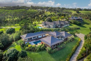 A large, multi-story house with a swimming pool, surrounded by lush greenery and a golf course.
