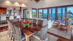 A spacious dining area with a large wooden table, woven chairs, and a view of the ocean. - Ikena Lani in Kilauea (Kilauea)