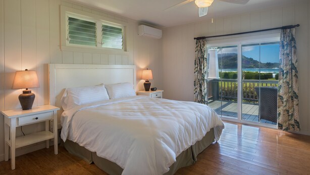 Ein Schlafzimmer mit einem großen Bett, zwei Nachttischlampen, einem Deckenventilator und Blick ins Freie durch eine Schiebetür.