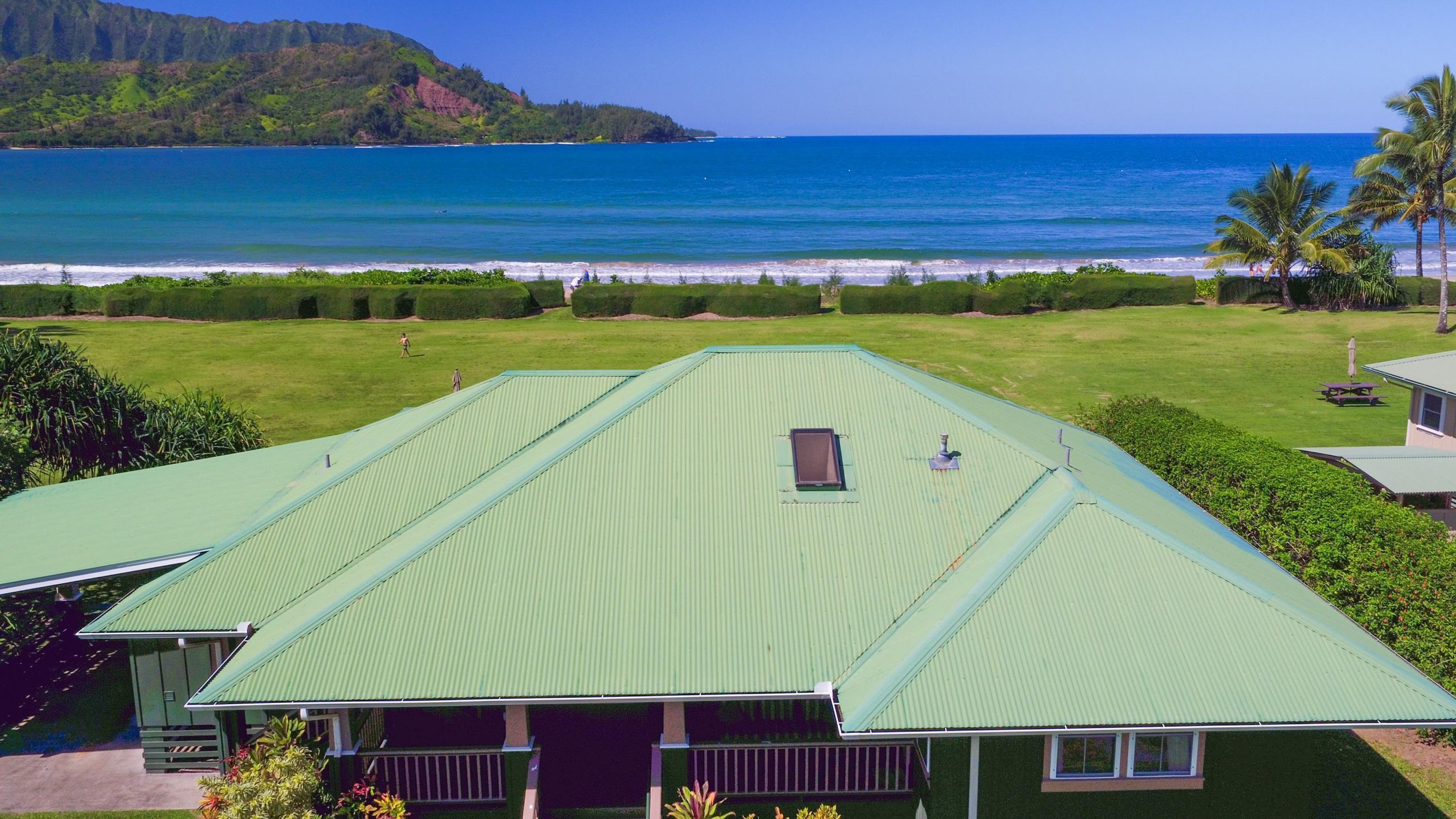 A large, green-roofed building with a view of the ocean and a lush landscape.