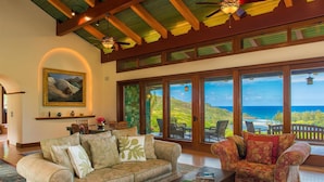 A spacious living area with a large window offering a view of the ocean, a ceiling fan, and a fireplace.