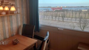Ein Zimmer mit Holztisch und Stühlen, einem Fenster mit Blick auf ein entferntes Gebäude und Bäume sowie einem Regal mit Dekoration.