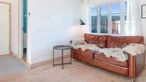 Ein Wohnzimmer mit einer braunen Ledersofa, einem kleinen runden Tisch und einem Fenster mit weißen Vorhängen.