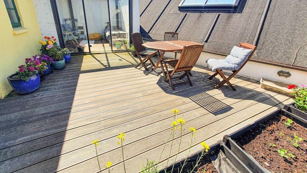 Eine Holzterrasse mit Tisch, Stühlen und Topfpflanzen, sowie einem Oberlicht.