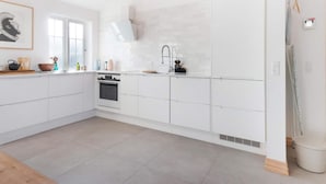 Eine moderne Küche mit weißen Schränken, einem eingebauten Backofen und einem großen Fenster.