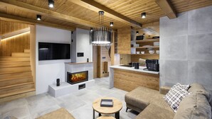 Una sala de estar moderna con chimenea, vigas de madera, un televisor de pantalla plana y un rincón de descanso acogedor.
