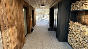 Un pasillo con paredes de madera y piso de baldosas, que conduce a una puerta y una pila de leña.