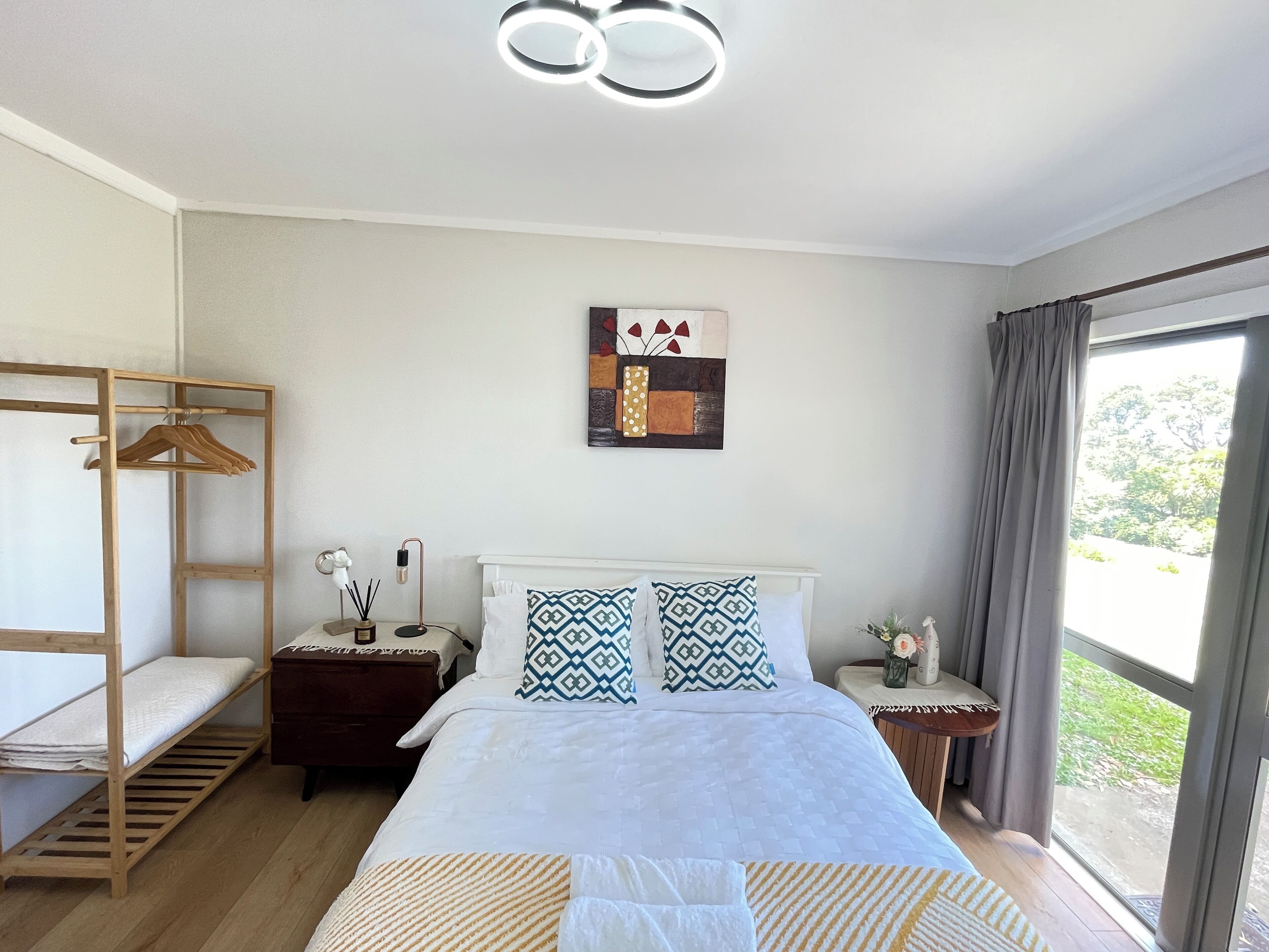 A bedroom with a bed, a wooden wardrobe, a bedside table with a lamp, and a window with curtains.