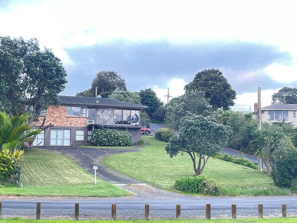 A residential area with a house featuring a balcony, a driveway, and surrounding greenery.