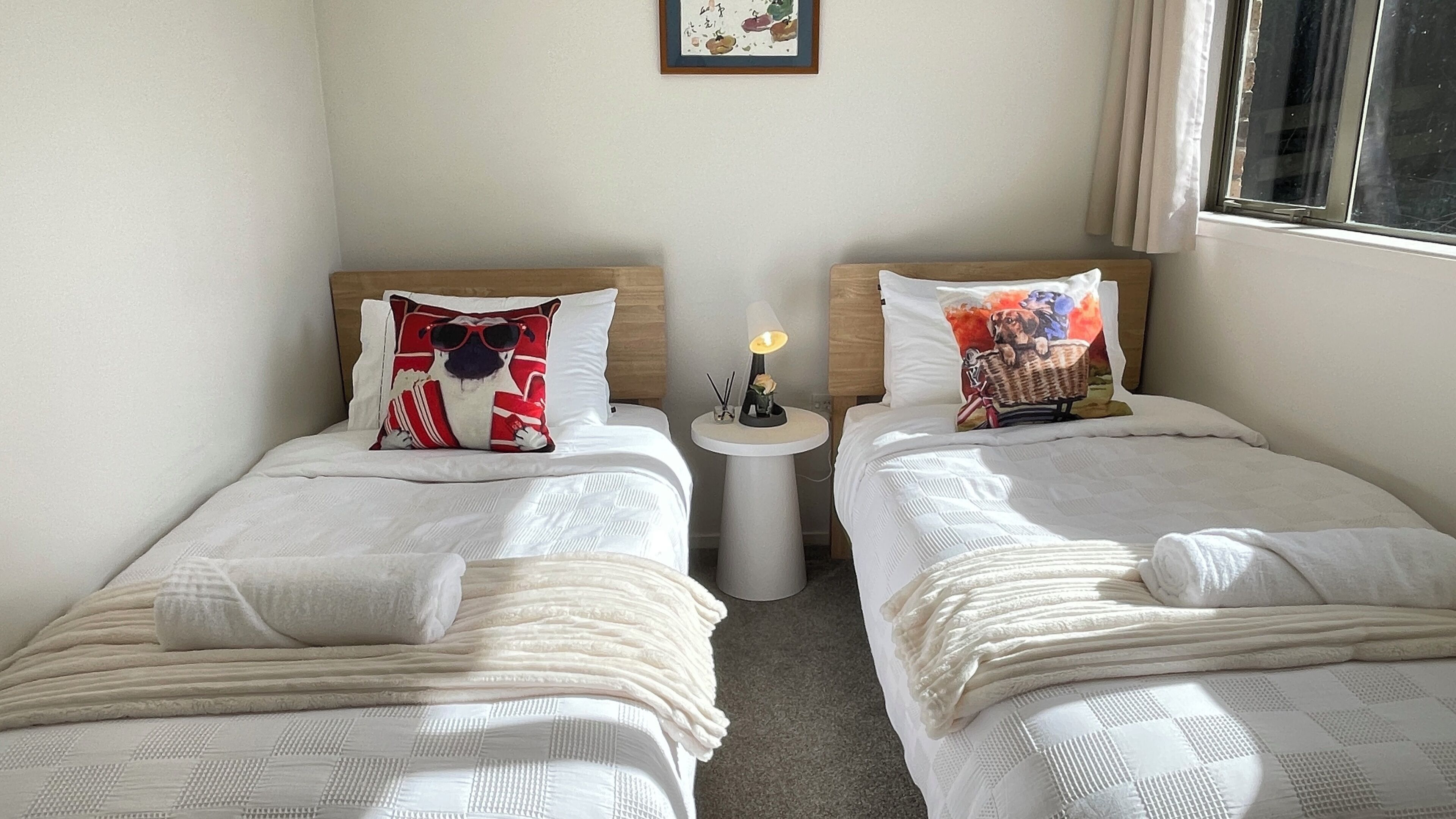 A hotel room with two single beds, each with a pillow and a bedside table with a lamp.