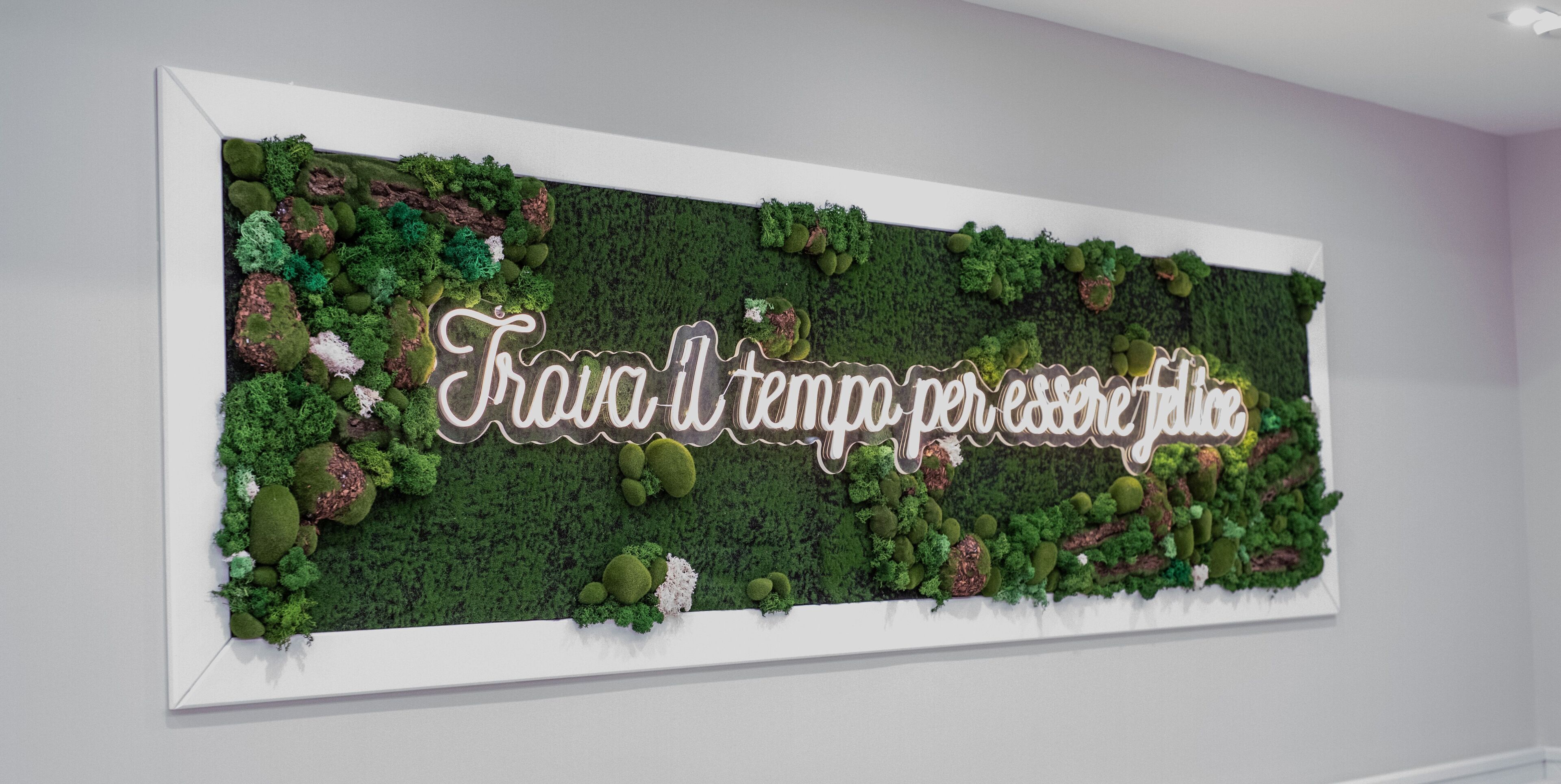 A wall with a green moss-like texture and a decorative sign that reads "Trava-l tempo per essere giace."