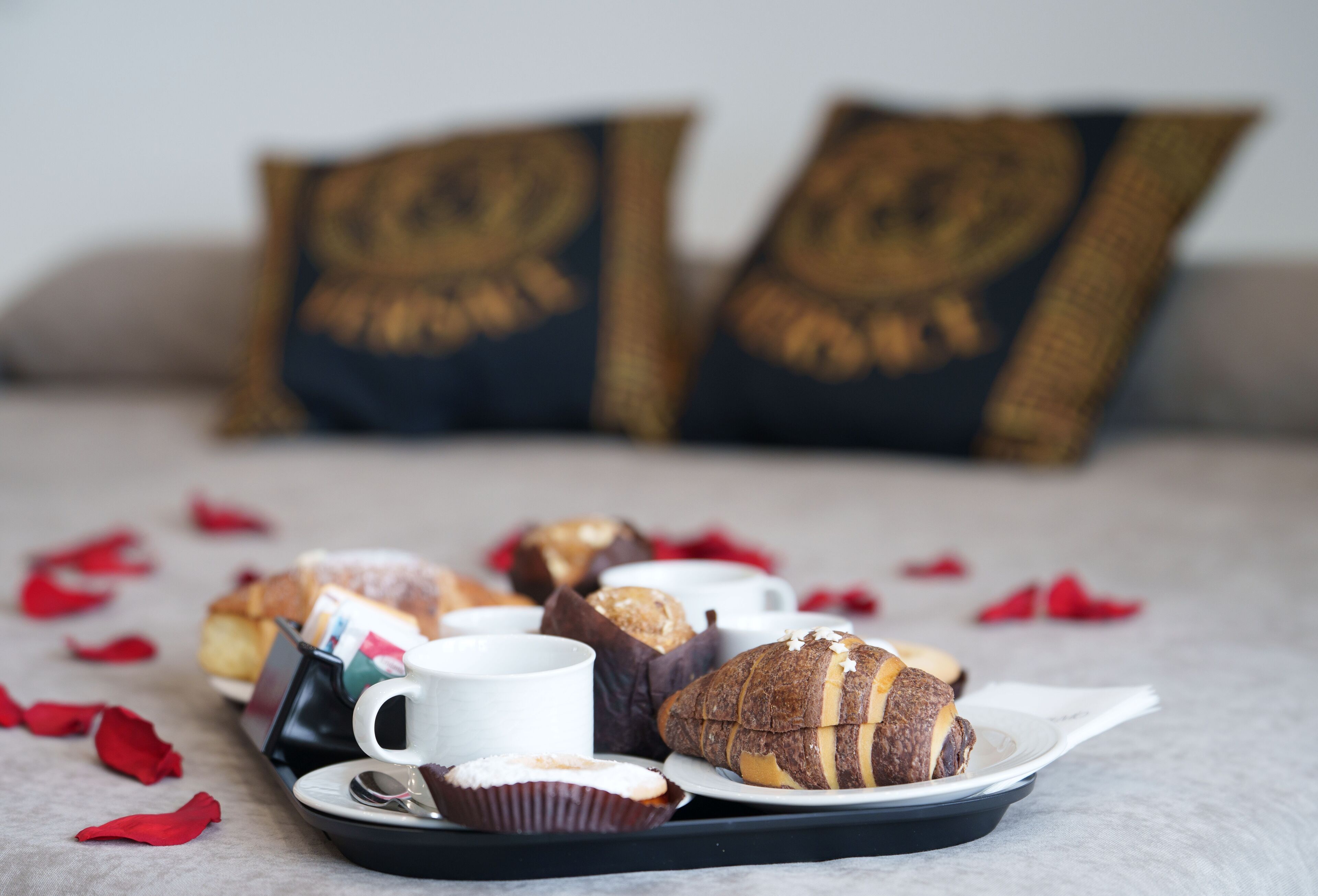 A tray with pastries and a cup on a table, with rose petals scattered around.