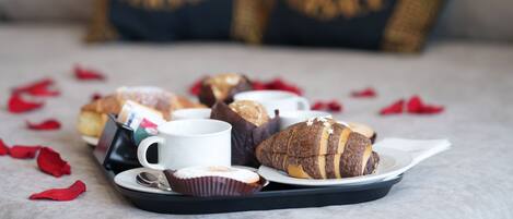 A tray with pastries and a cup on a table, with rose petals scattered around.