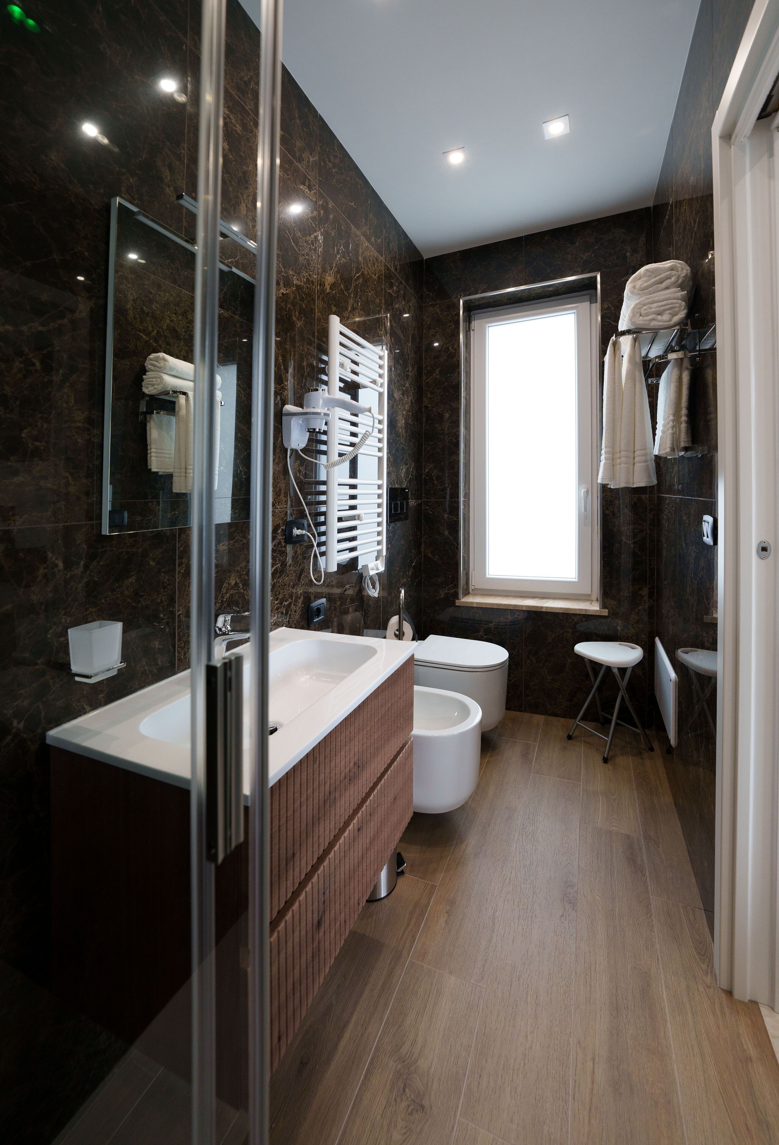 Ein modernes Badezimmer mit Duschkabine aus Glas, einem doppelten Waschtisch, einer Toilette und einem Fenster für natürliches Licht.