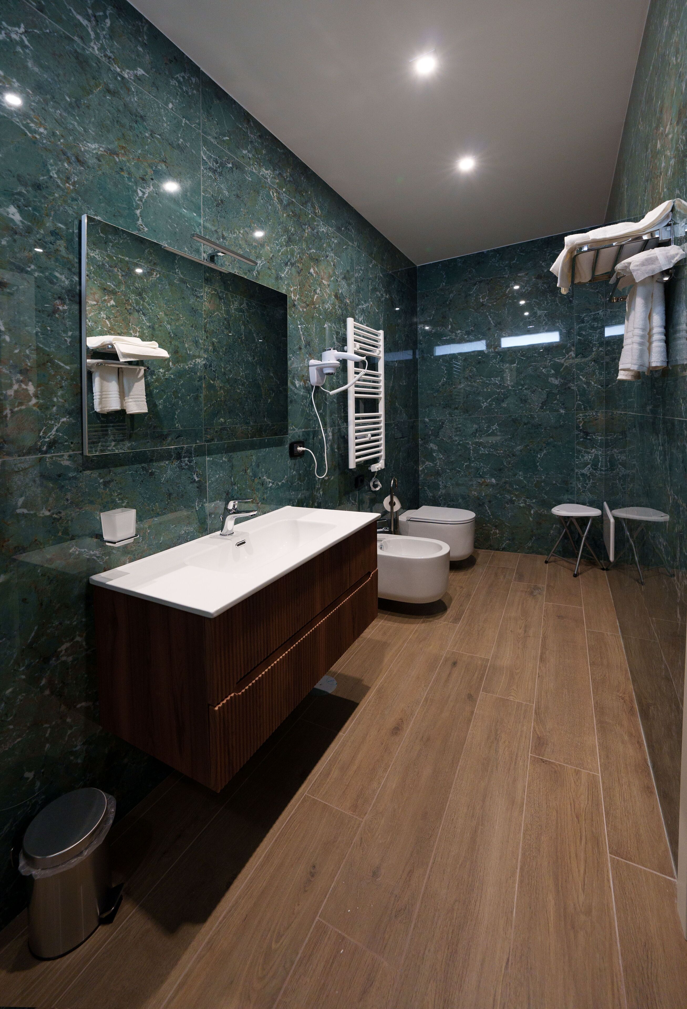 A modern bathroom with a marble wall, a large sink, a toilet, and a bidet.