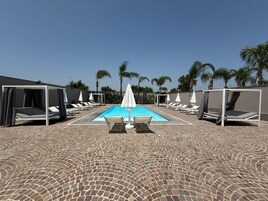 Un área de piscina con una piscina rectangular, sillones de descanso y sombrillas.