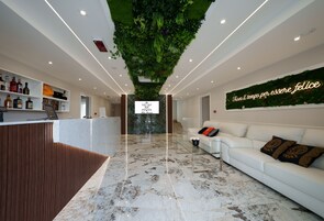 Un área de recepción moderna con piso de mármol, un mostrador de recepción, un sofá blanco y una pared con jardín vertical y un letrero de neón.