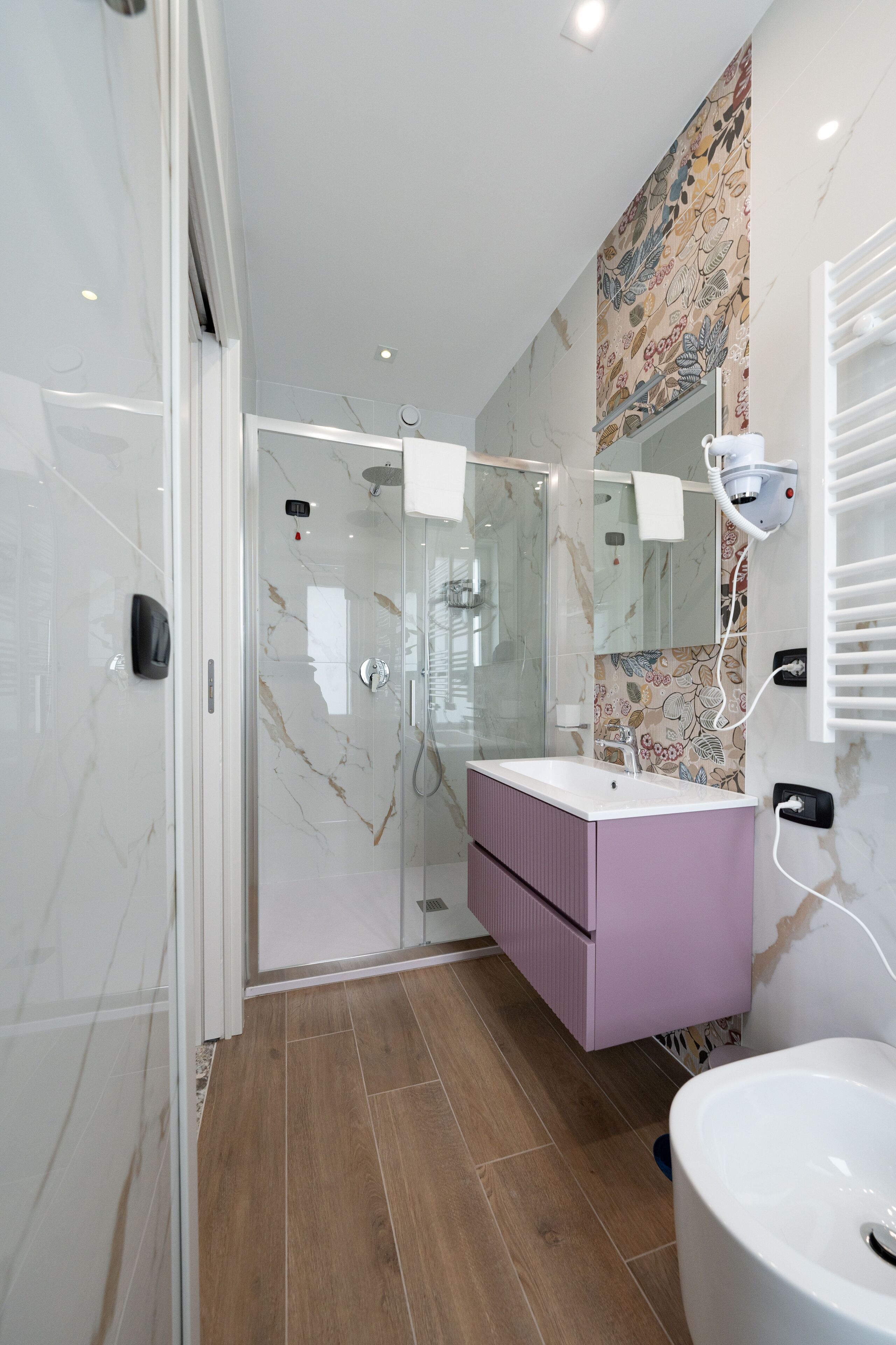 Un baño moderno con cabina de ducha de vidrio, un lavabo con tocador morado y un espejo grande.