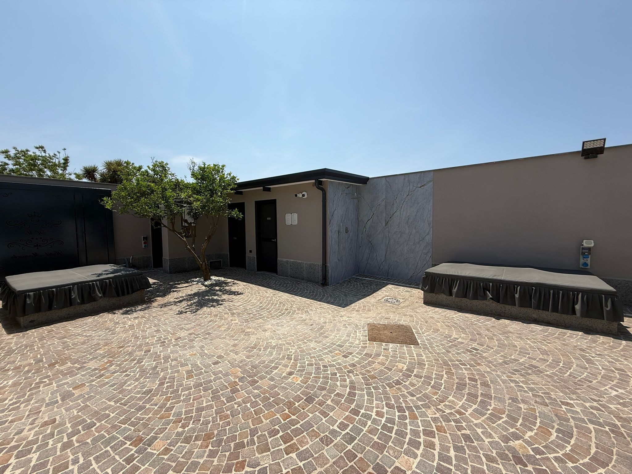 A courtyard with a tiled floor, a covered seating area, and a small tree.