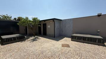 A courtyard with a tiled floor, a covered seating area, and a small tree.