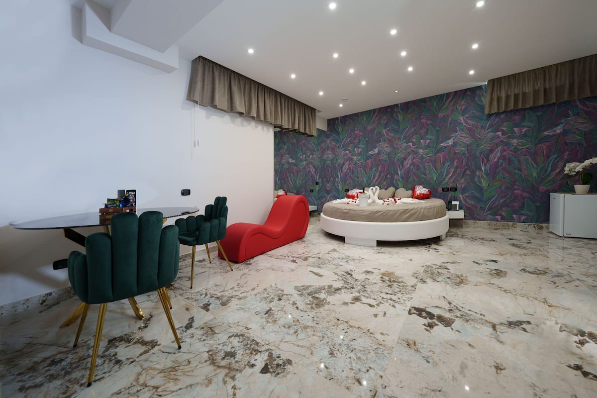 Een moderne slaapkamer met een rond bed, een zithoek met een tafel en stoelen, en een levendig behang met bloemen.
