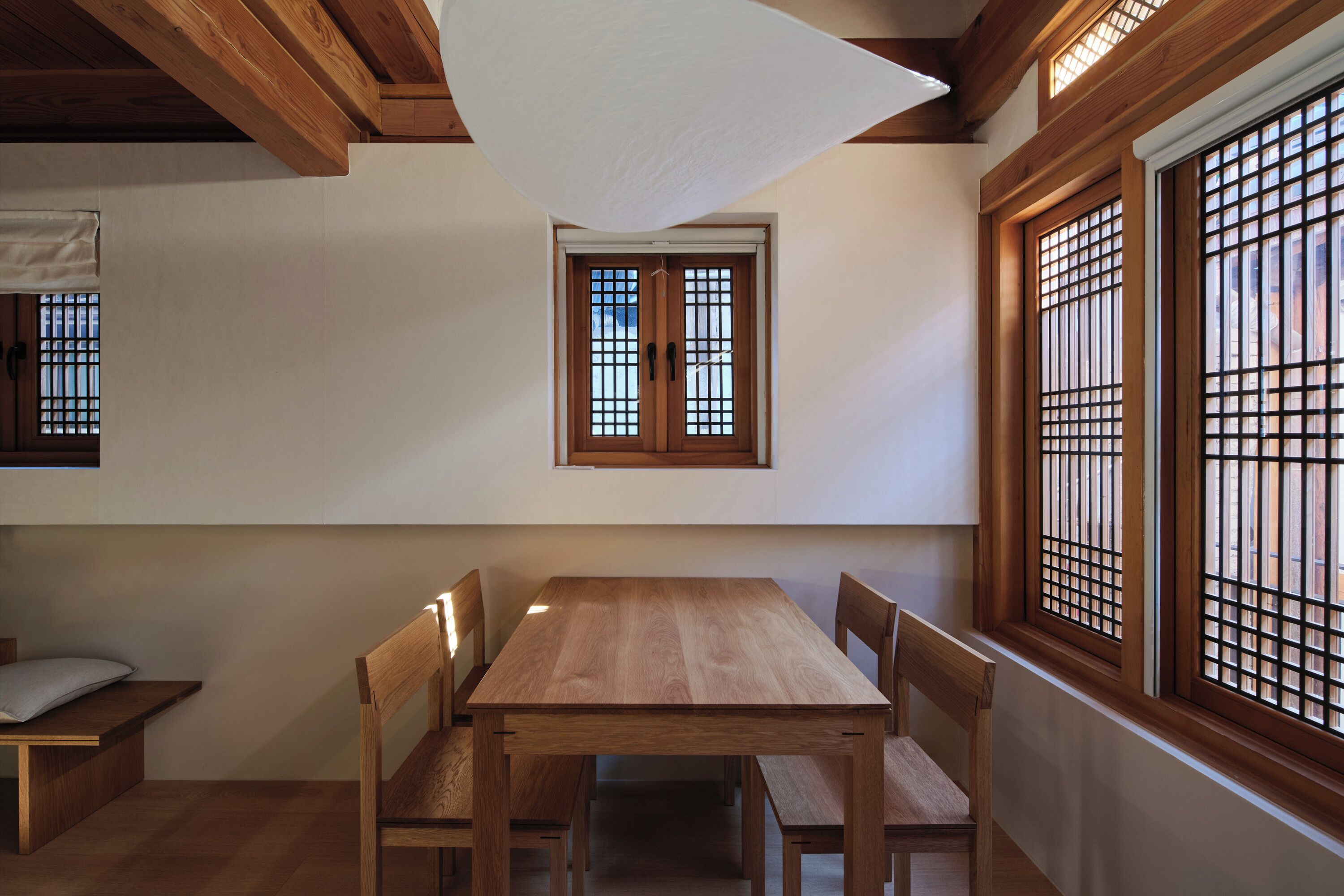 A dining area with a wooden table and chairs, a window with a grid pattern, and a ceiling light fixture.