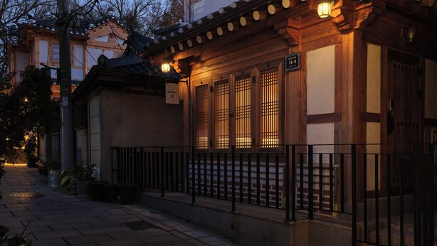 En traditionel japansk bygning med en træfacade, et tagtækket tag og en lille veranda med gelænder i sort.