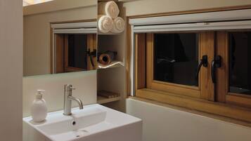 A bathroom with a white sink, a mirror, wooden beams on the ceiling, and a window with wooden shutters.