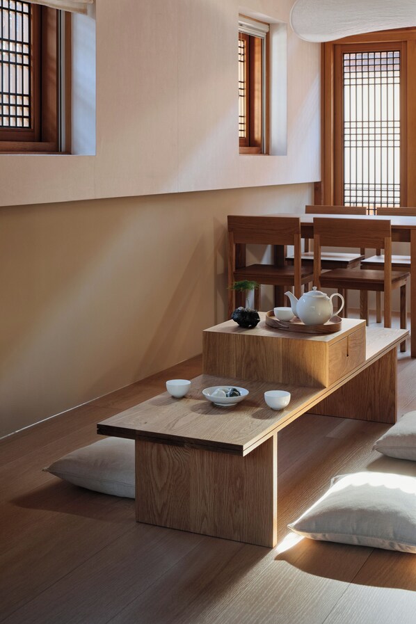 Un coin repas minimaliste en bois, avec une table dressée pour le thé, des chaises en bois et une vue sur l’extérieur à travers une fenêtre à carreaux.