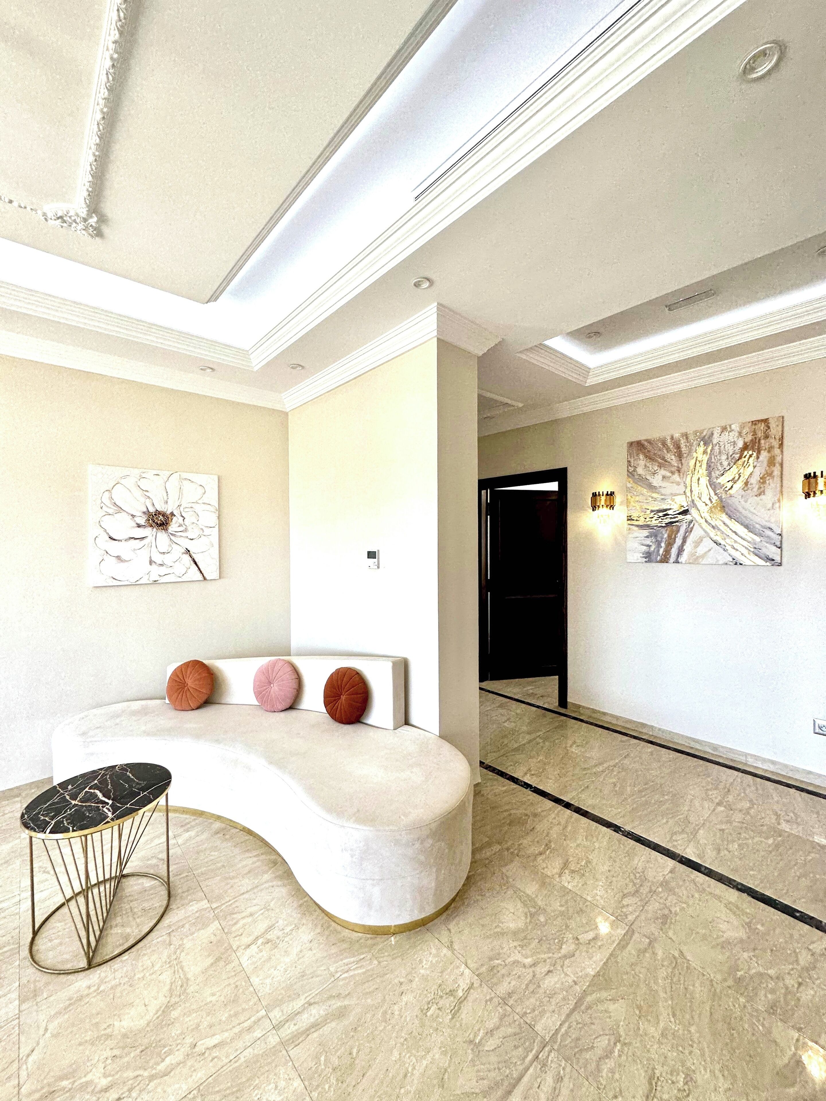 Un lobby moderno con un mostrador de recepción blanco, piso de mármol y dos lámparas fijadas a la pared.