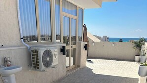 A rooftop patio with a tiled floor, a water fountain, an air conditioning unit, and potted plants.