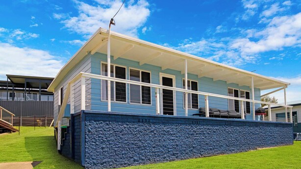 Ein modernes Haus mit überdachter Veranda, rustikalem Sockel und gepflegtem Rasen.