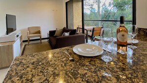 Une cuisine moderne avec des comptoirs en granit, un coin repas avec une table et des chaises, un canapé et une grande fenêtre donnant sur les arbres.