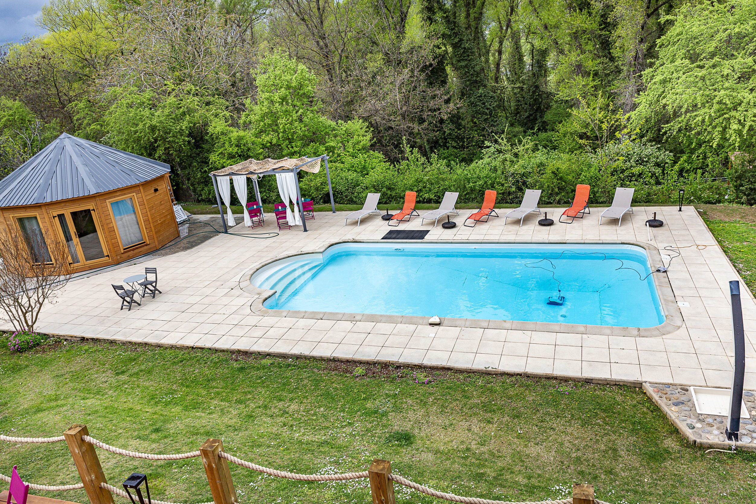 A backyard with a swimming pool, lounge chairs, a gazebo, and a wooden building.