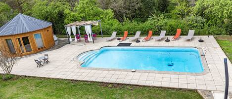 A backyard with a swimming pool, lounge chairs, a gazebo, and a wooden building.