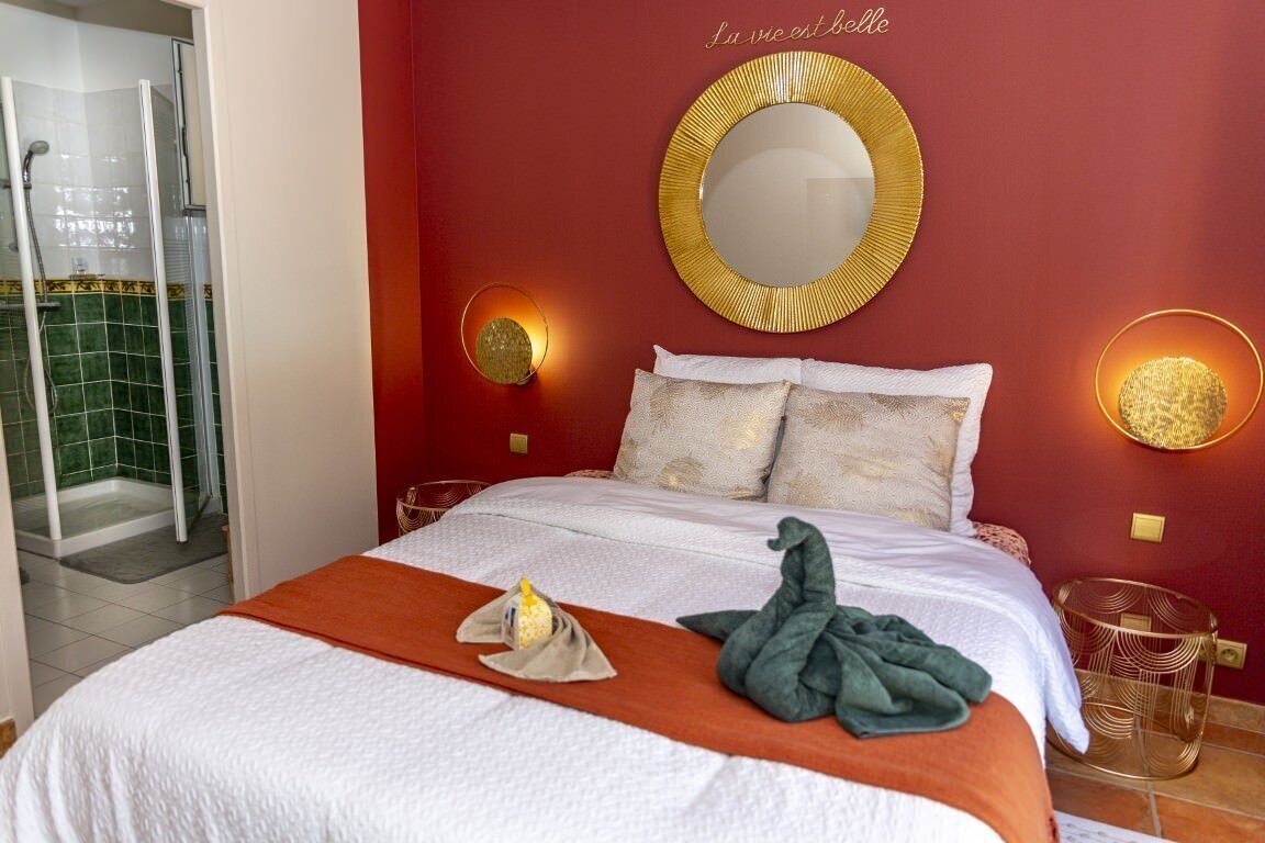 Habitación de hotel con cama, espejo redondo, dos apliques y zona de ducha.