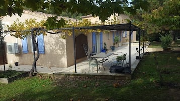 A covered patio with a table and chairs, a pergola, and a building with blue shutters.